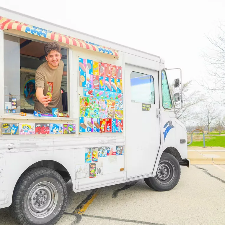 A server leaning out of the truck window, smiling and holding out a wrapped ice cream bar.